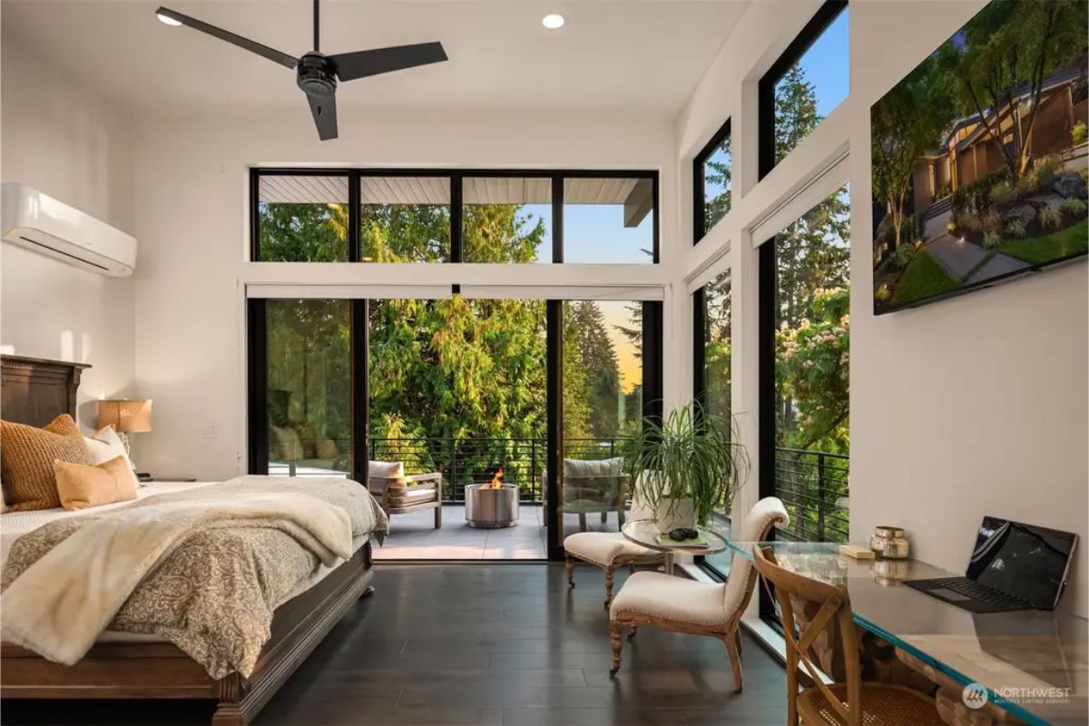 Luxurious master bedroom with floor-to-ceiling windows, a private balcony, and a seating area overlooking lush greenery. 