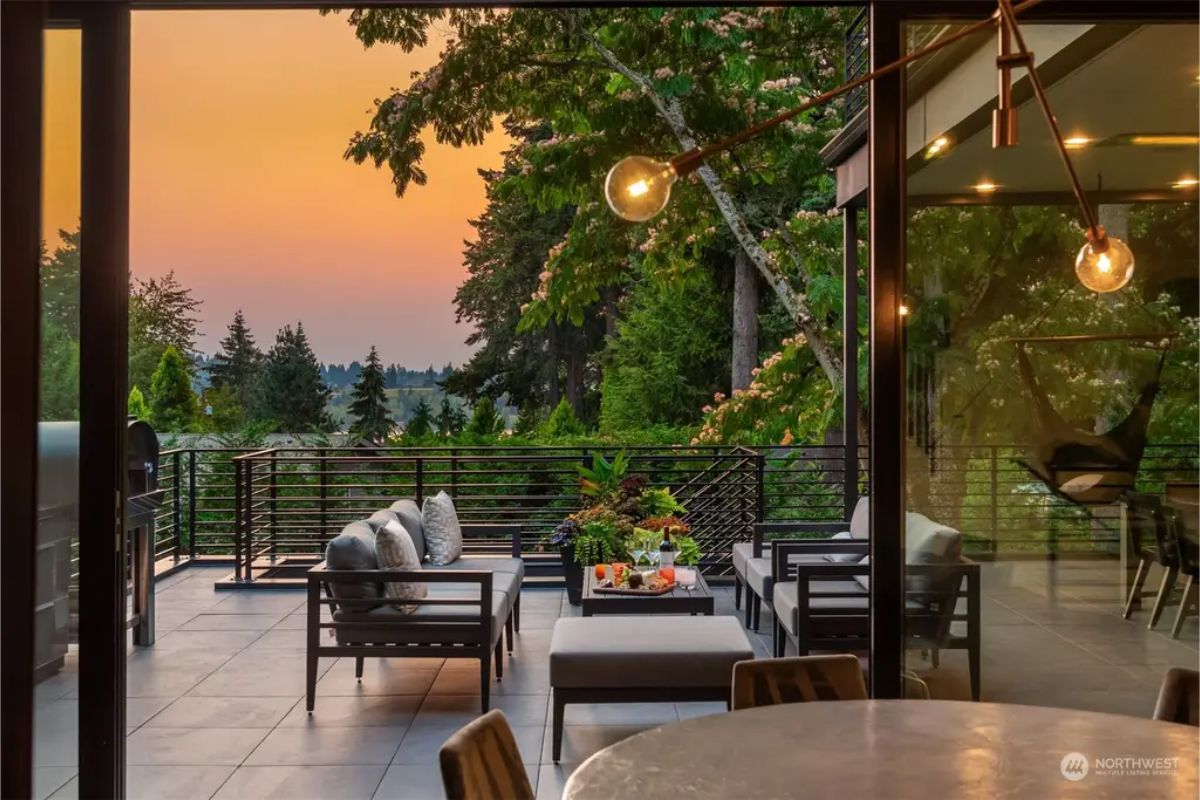 Outdoor terrace with a seating area, ambient lighting, and a beautiful sunset view over a forested landscape. 