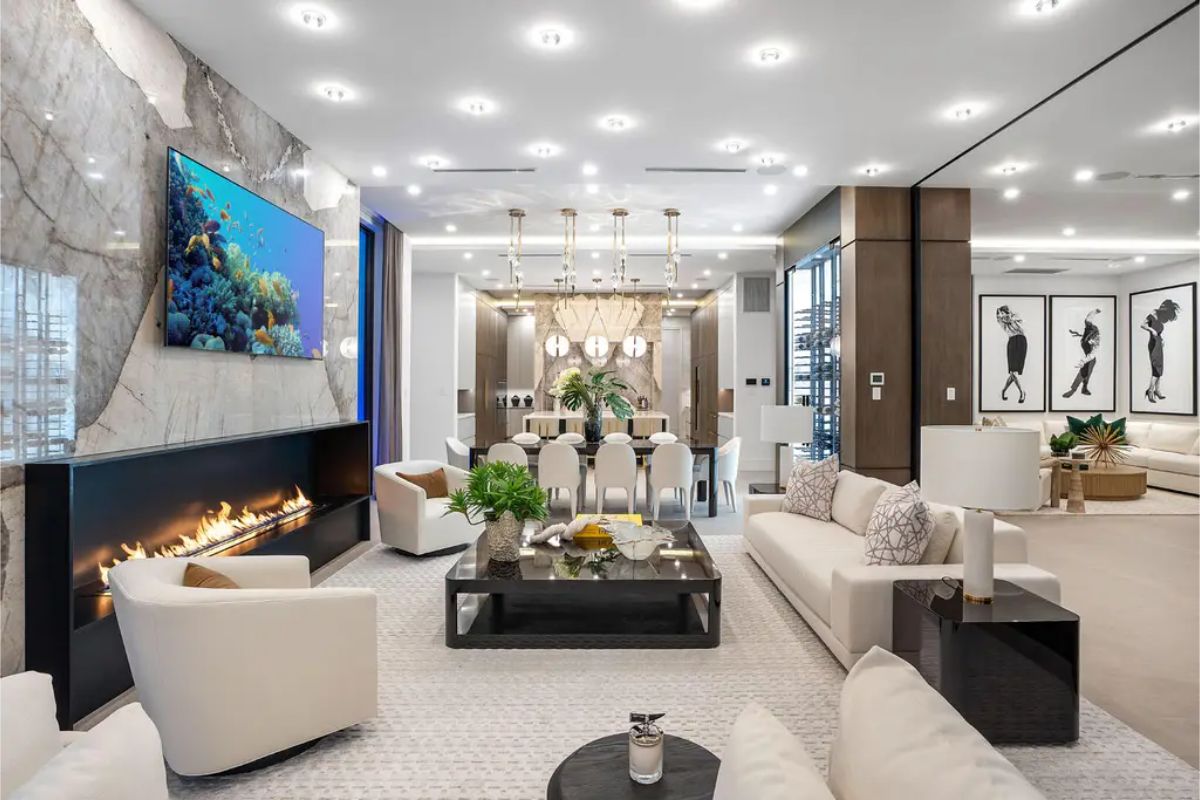 Modern living room with plush white seating, a sleek black coffee table, a linear fireplace, and a large aquarium-themed TV display. 