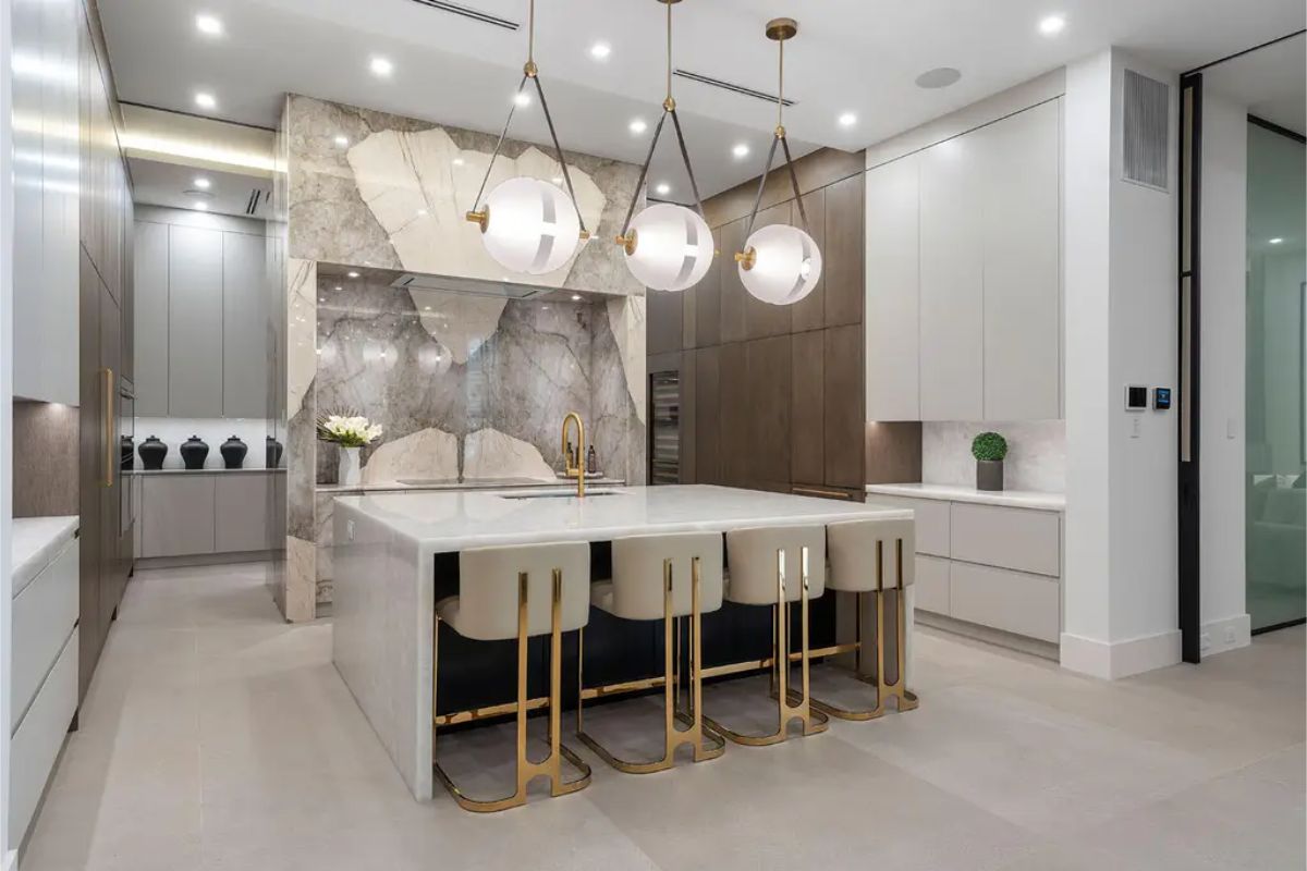 Minimalist kitchen design with a large marble island, gold-accented bar stools, and geometric pendant lighting. 
