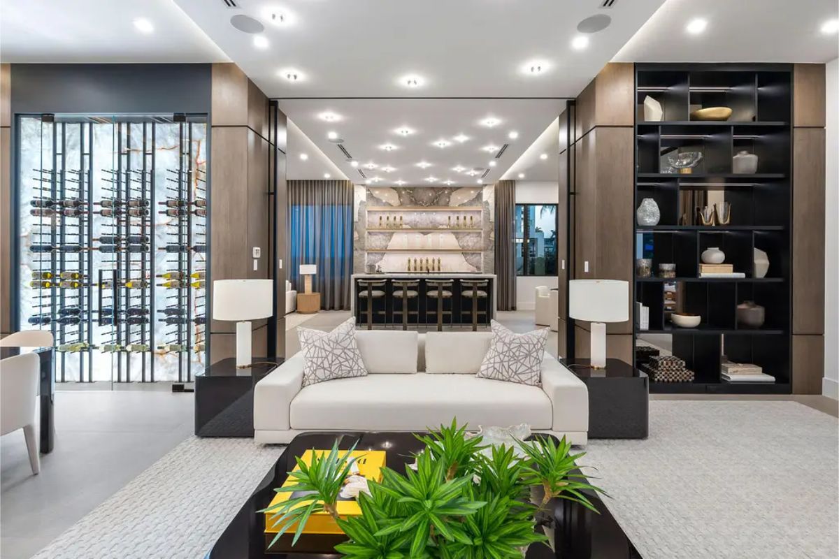 Elegant lounge area featuring a white sofa with patterned cushions, flanked by black shelving units and a sophisticated bar setup in the background. 