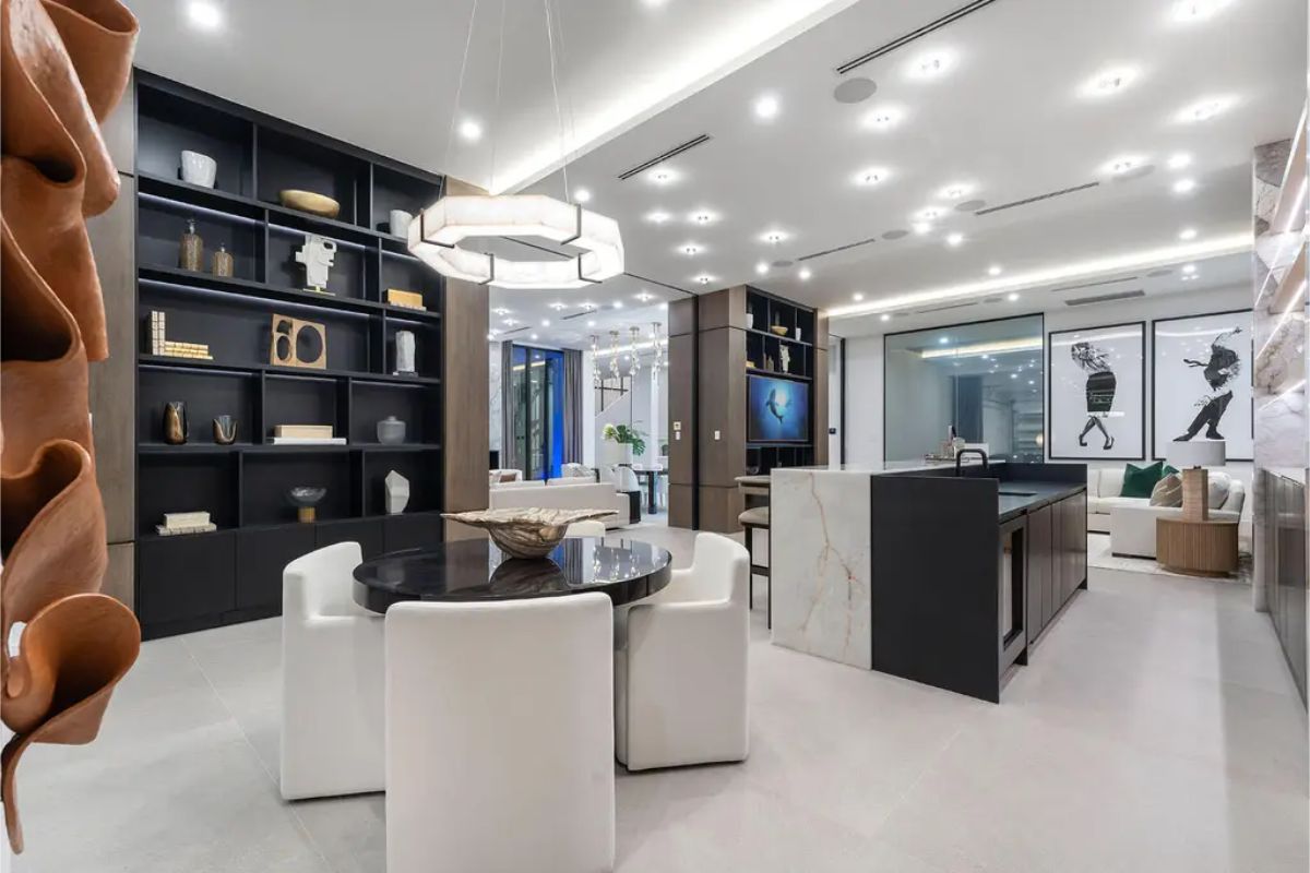 Open-concept space with a cozy round dining table, modern shelving, and a view into the sleek kitchen and living areas. 