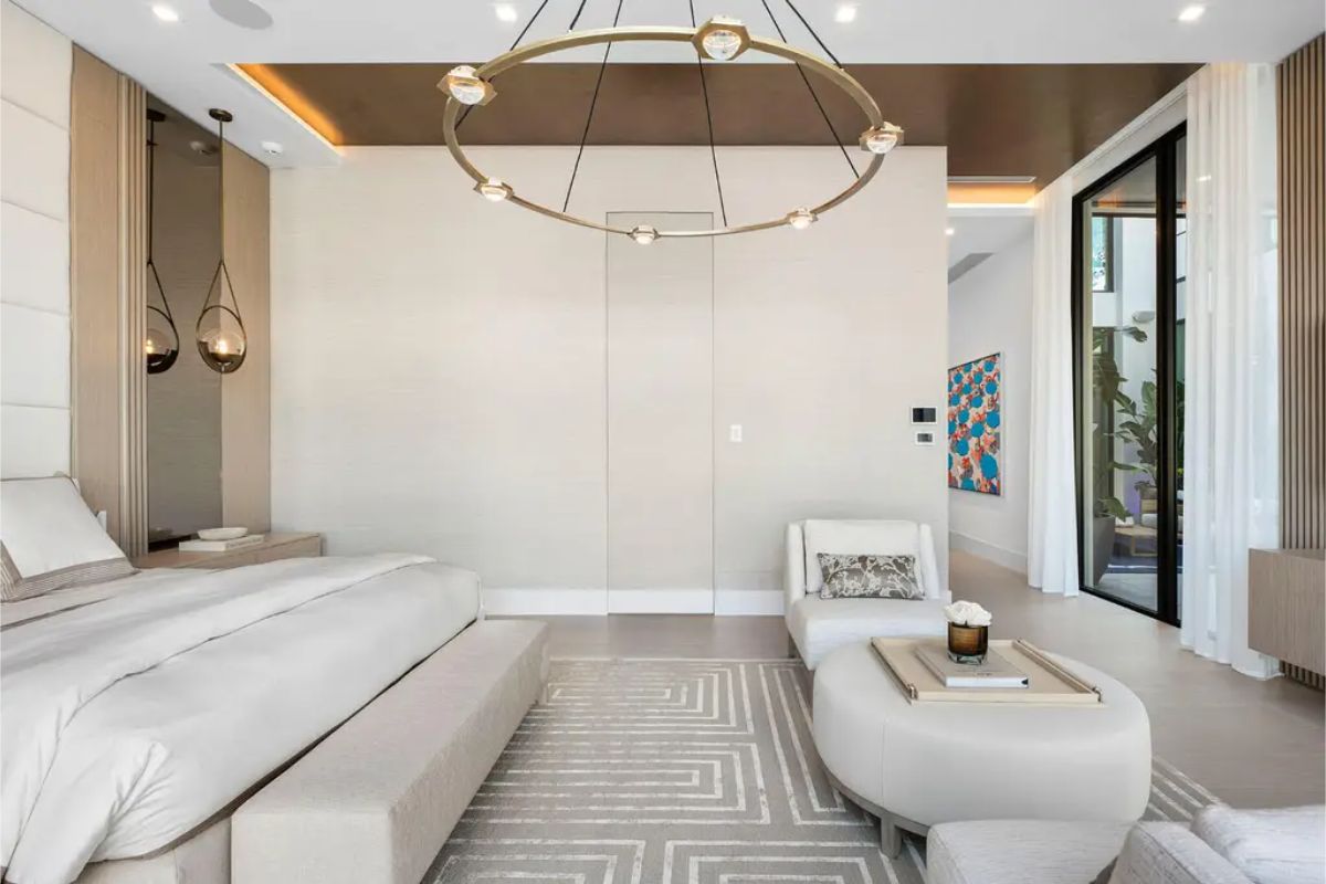 Serene bedroom interior featuring a large upholstered bed, modern ring chandelier, and a neutral color palette with subtle accents. 