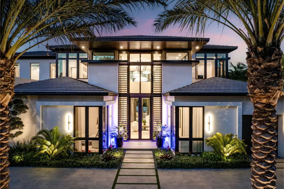 Grand entrance of a contemporary home with large windows, symmetrical design, and vibrant landscape lighting. 
