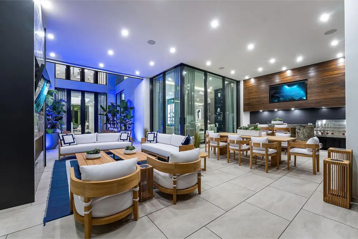 Spacious outdoor entertainment area with dining and lounging furniture, a built-in grill, and overhead lighting for evening gatherings. 