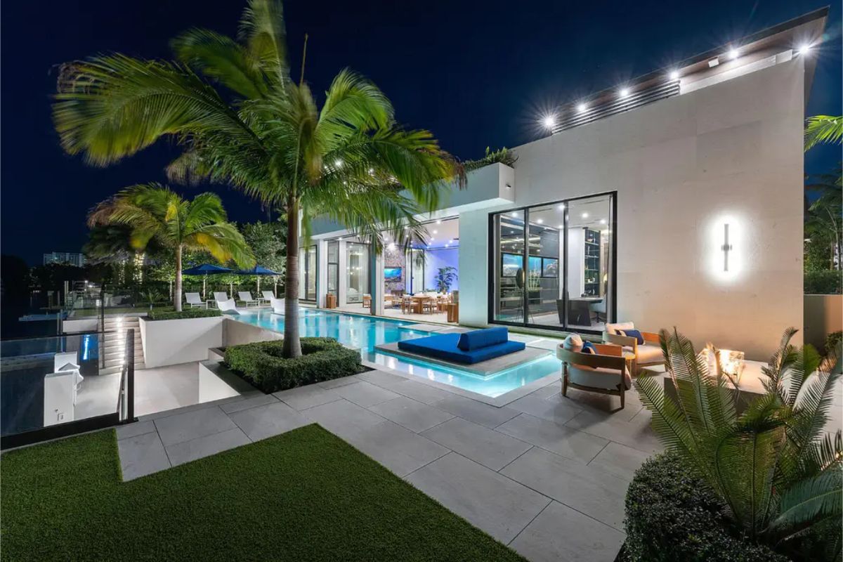 Stylish poolside setting with cozy seating, vibrant lighting, and lush greenery creating a serene nighttime atmosphere. 