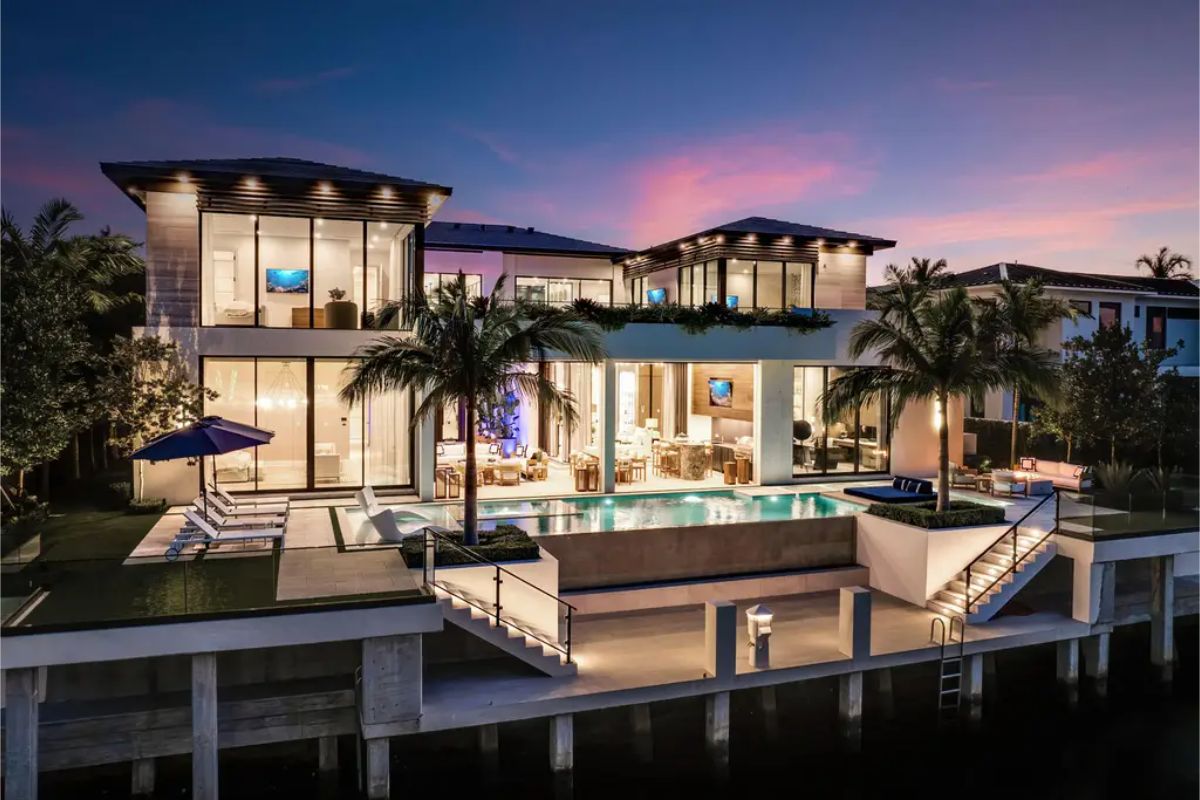 Stunning waterfront villa showcases expansive glass walls, an infinity-edge pool, and vibrant twilight colors enhancing its modern architecture. 