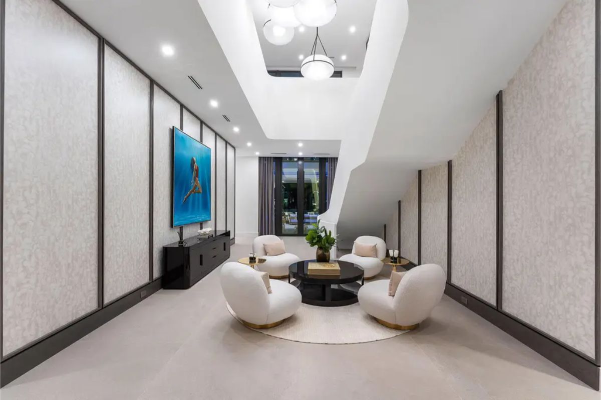 Stylish indoor seating area with plush white chairs arranged around a circular rug beneath a floating staircase. 