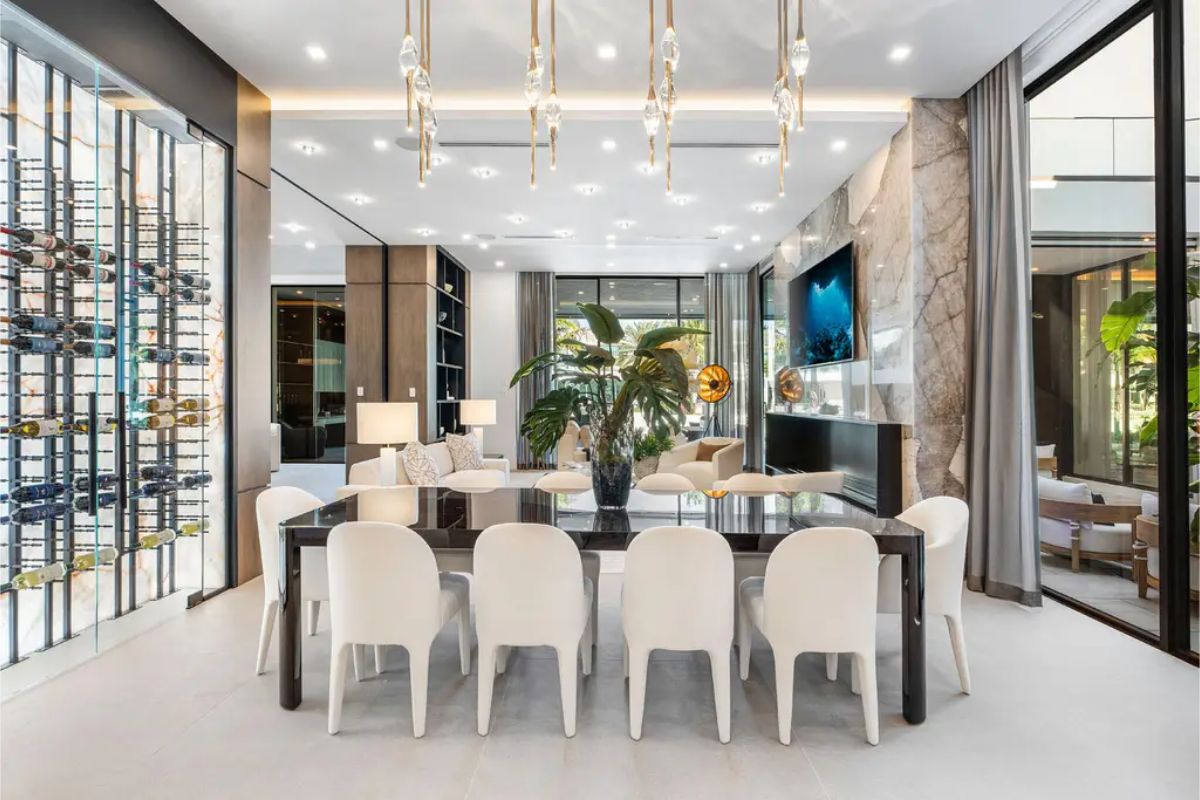 Luxurious dining room with statement pendant lights, a black dining table, and a backdrop of a stunning wine rack and floor-to-ceiling windows. 
