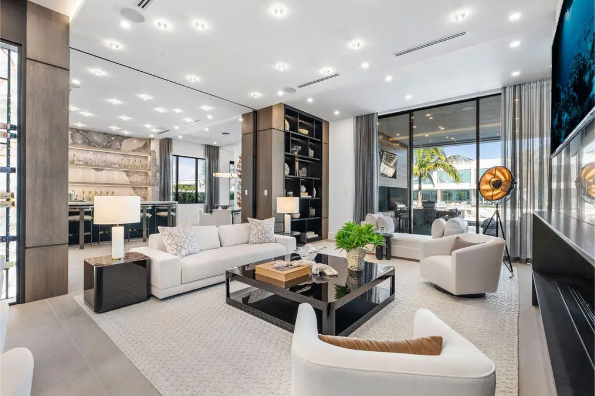 Spacious and bright lounge with white sofas, modern decor, and a view of the outdoor entertainment area. 