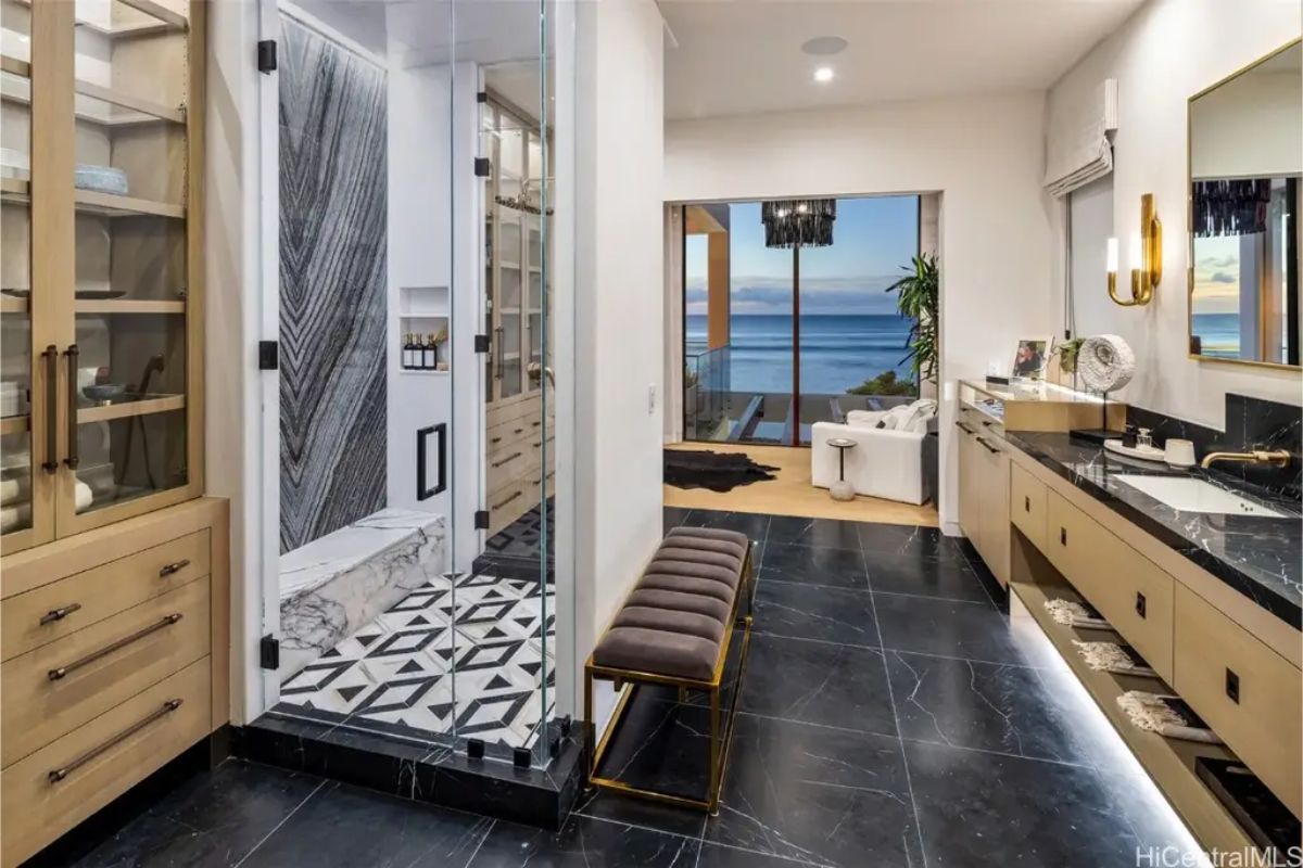 Elegant bathroom with a glass-enclosed shower, black marble flooring, and a direct view of the ocean. 