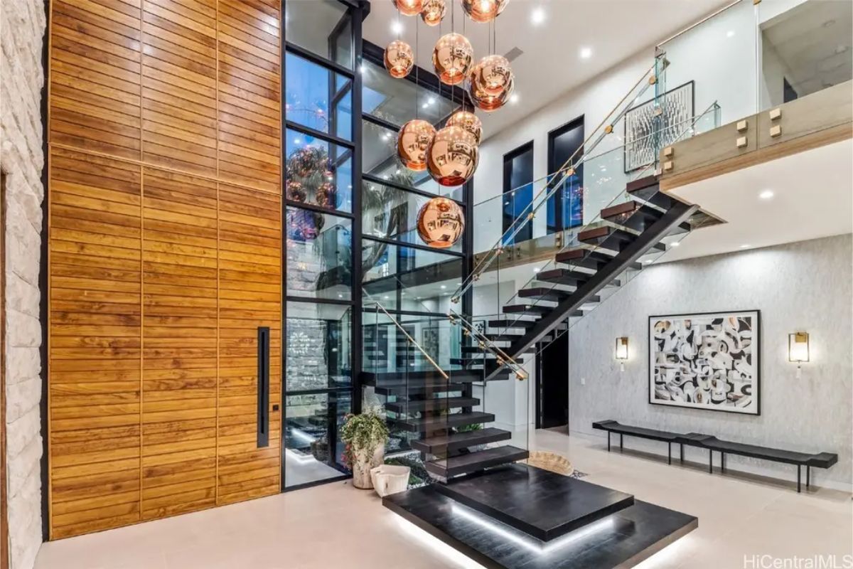 Grand entrance showcases a floating staircase, wooden paneling, and oversized copper pendant lights. 