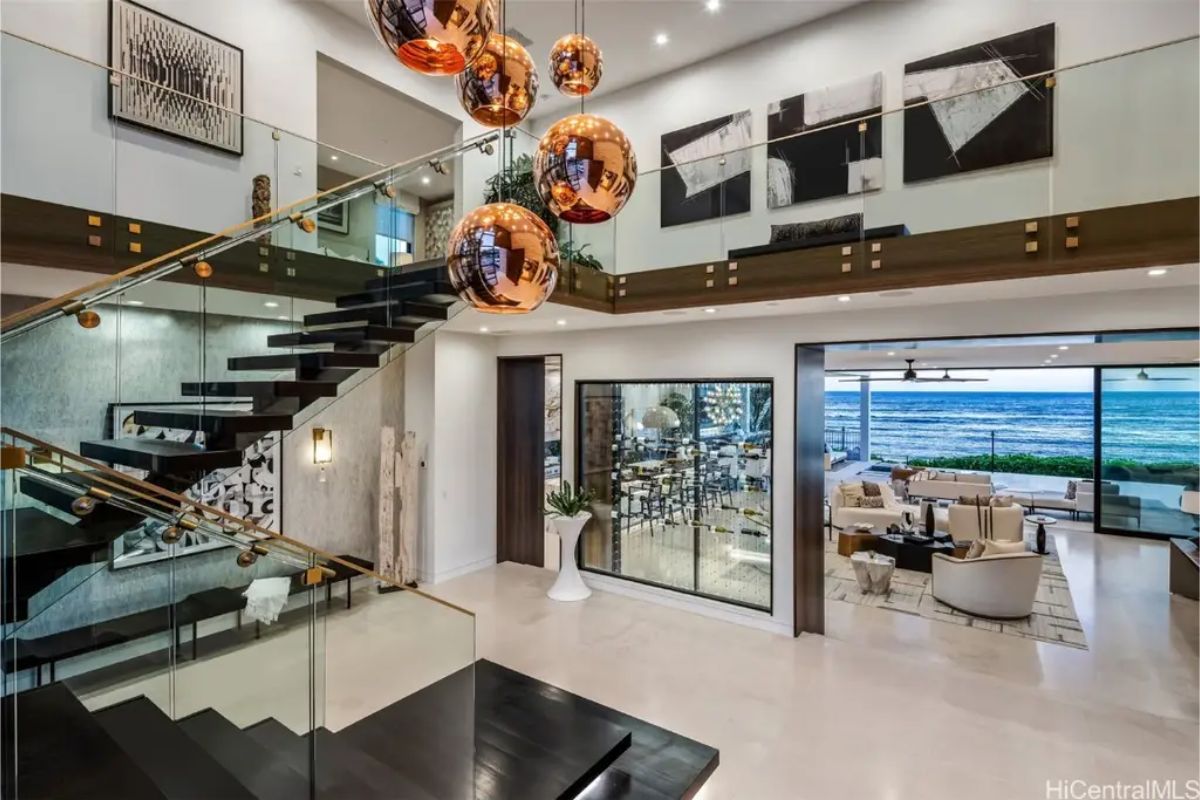 Open-concept living area highlights contemporary black metal stair railings, ocean views, and high-end décor. 