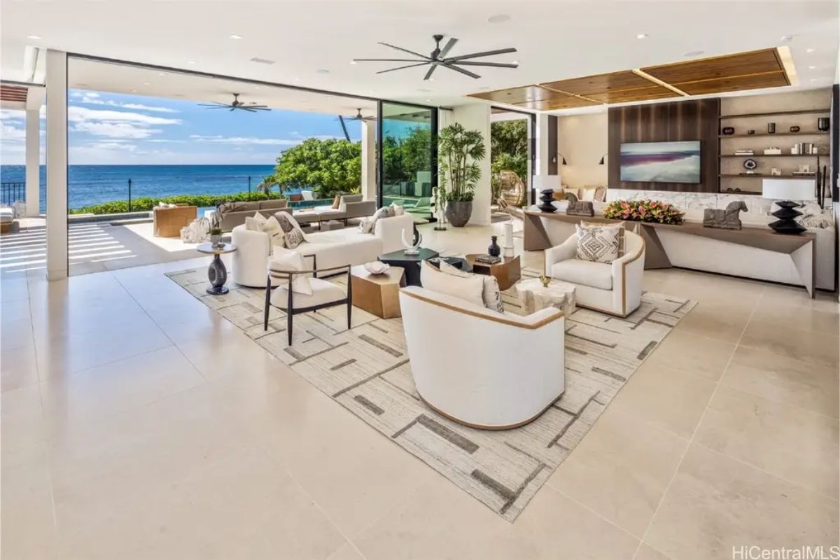 Expansive indoor-outdoor living space seamlessly blends with the ocean backdrop, featuring plush seating and a neutral color palette. 