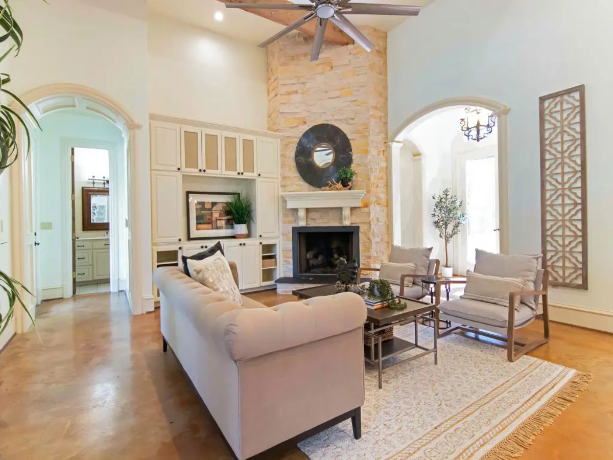 Living room with a tall stone fireplace, built-in cabinetry, and high ceilings.