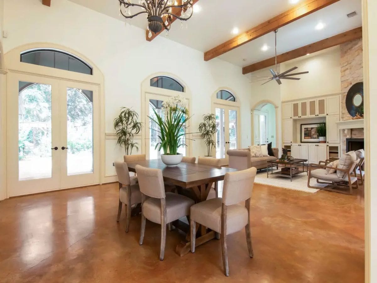 Open-concept space with a dining area and living room under exposed wooden beams.
