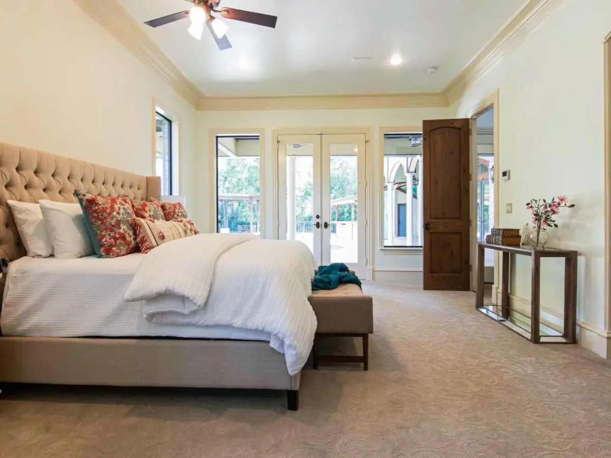 Bedroom with a tufted beige bed, white bedding, and floral accent pillows.