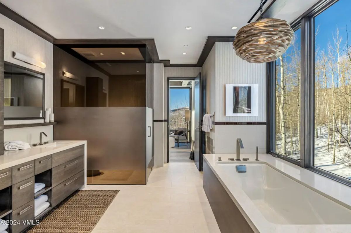 Offers a sleek freestanding bathtub positioned by floor-to-ceiling windows overlooking a snowy landscape.