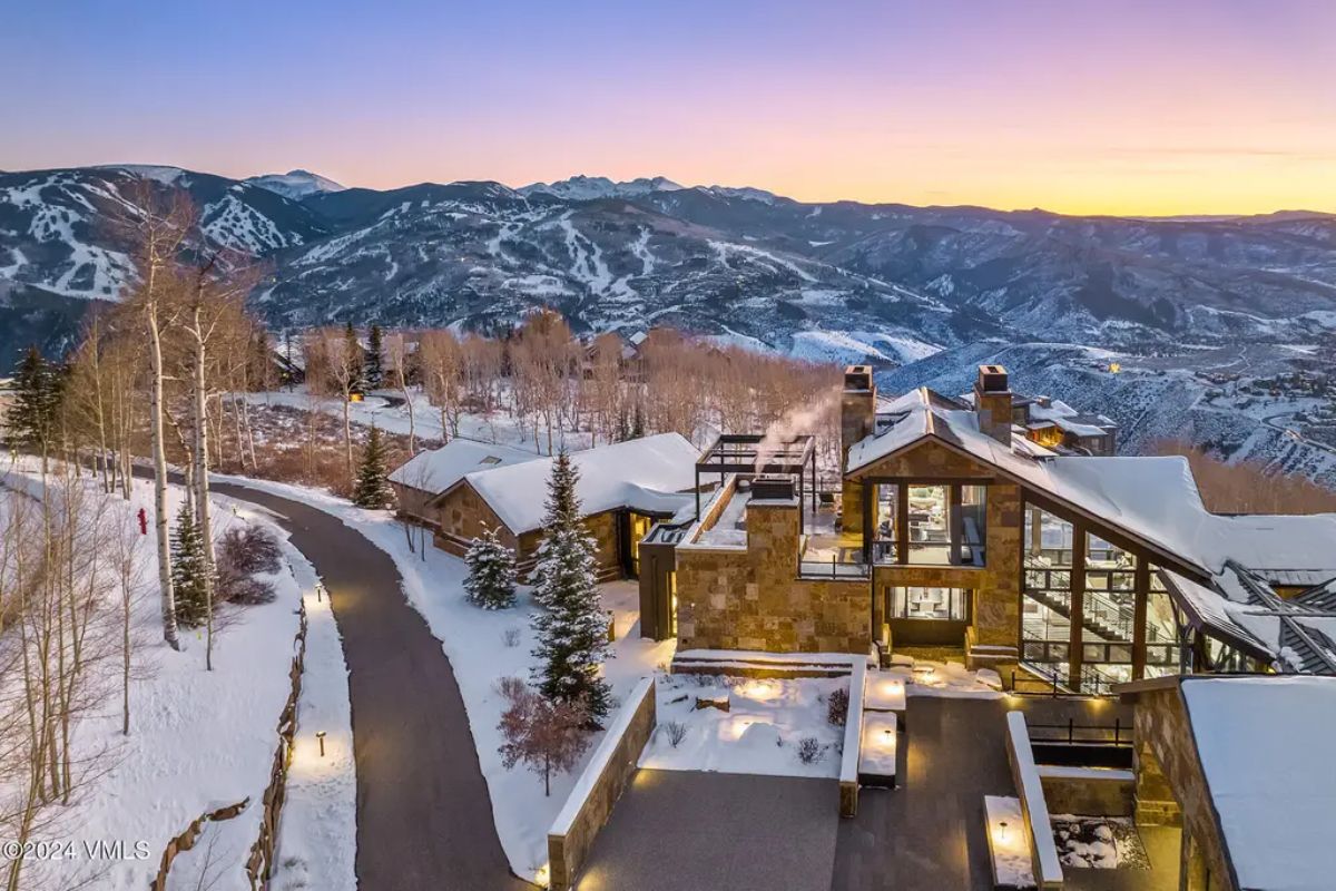 Positioned on a snow-covered hillside, the home offers sweeping views of mountain peaks and ski slopes.