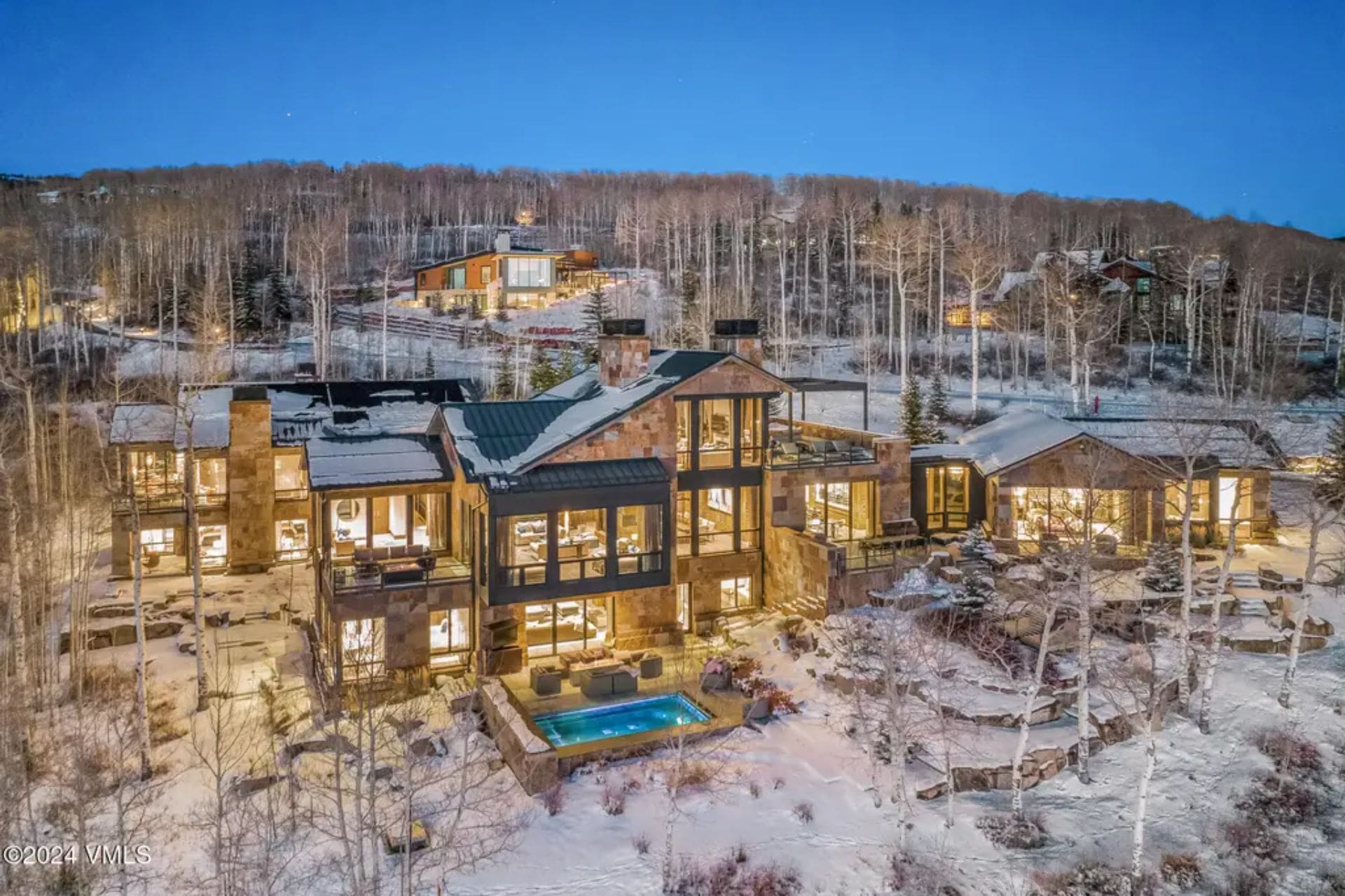 Large multi-level home with extensive glass windows, surrounded by snow-covered landscape and sparse trees.