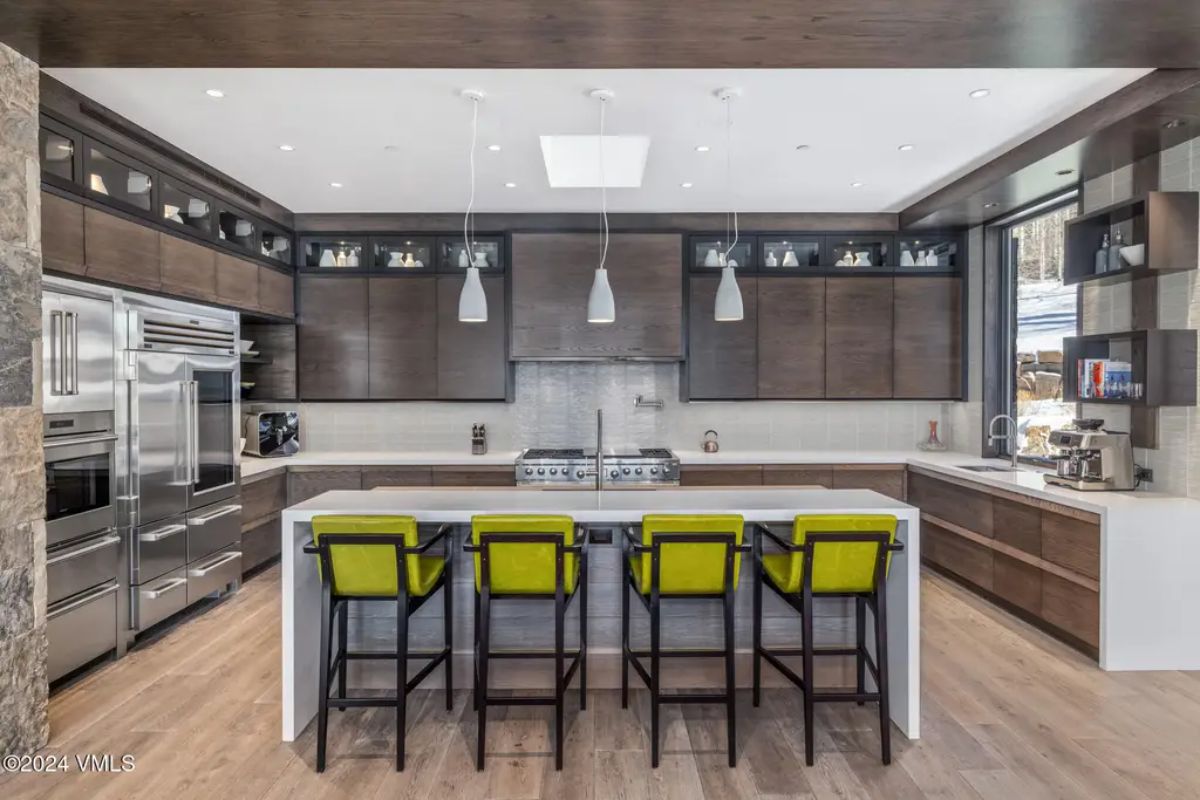 Dark wood cabinetry and sleek stainless steel appliances contrasts with bright green bar stools at the central island.