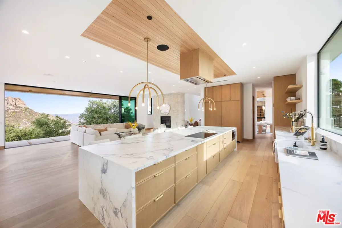 A large marble island, light wood cabinetry, and gold pendant lighting.