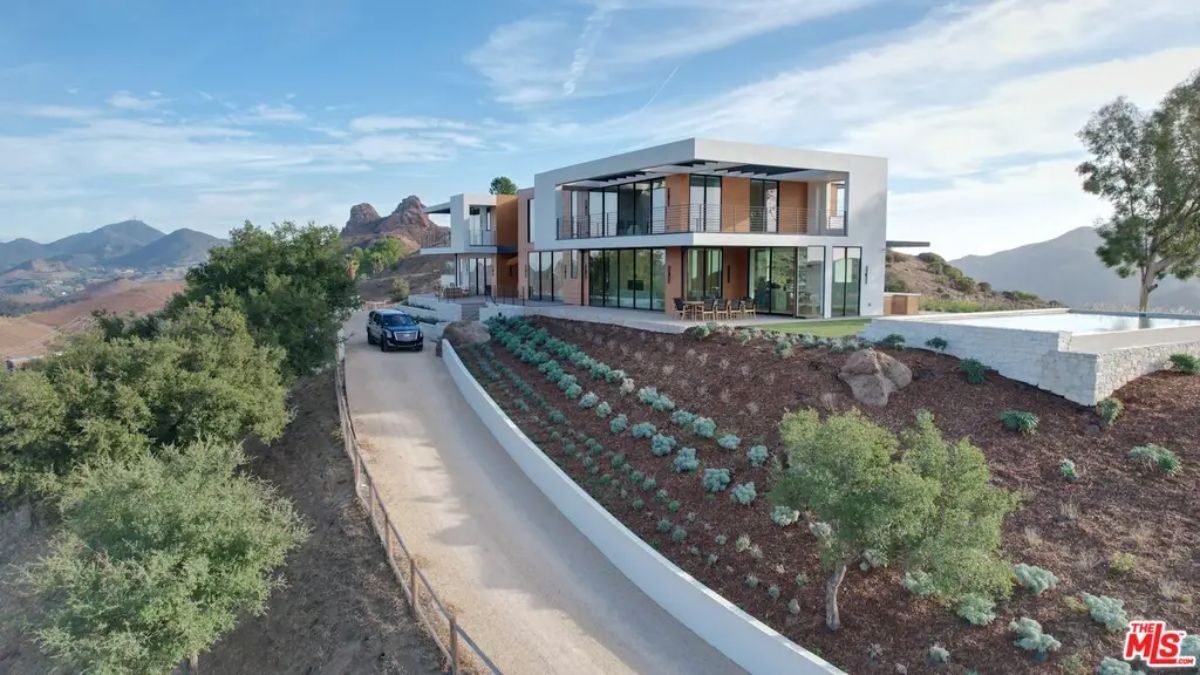 Two-story contemporary home sits on a sloped landscape with a winding driveway.