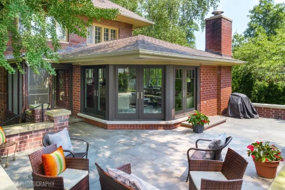 French doors lead from an enclosed sunroom to a spacious patio with outdoor seating.