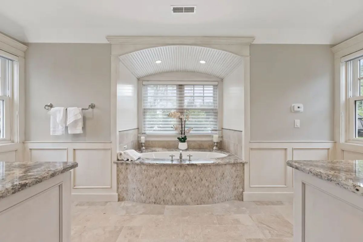 Built-in soaking tub with a marble surround, framed by an arched alcove with beadboard detailing and recessed lighting.