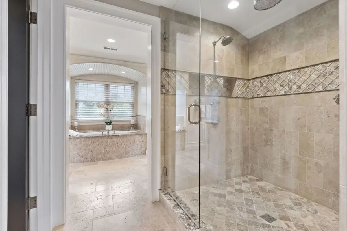 Walk-in shower features floor-to-ceiling natural stone tiles, accented by a decorative mosaic trim.