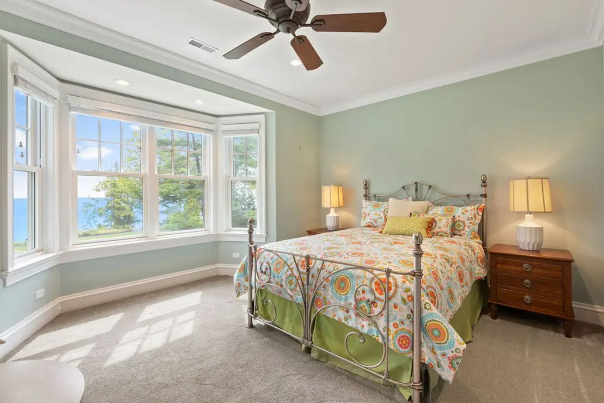 Bedroom showcases a large bay window with panoramic views of greenery and a serene lake.