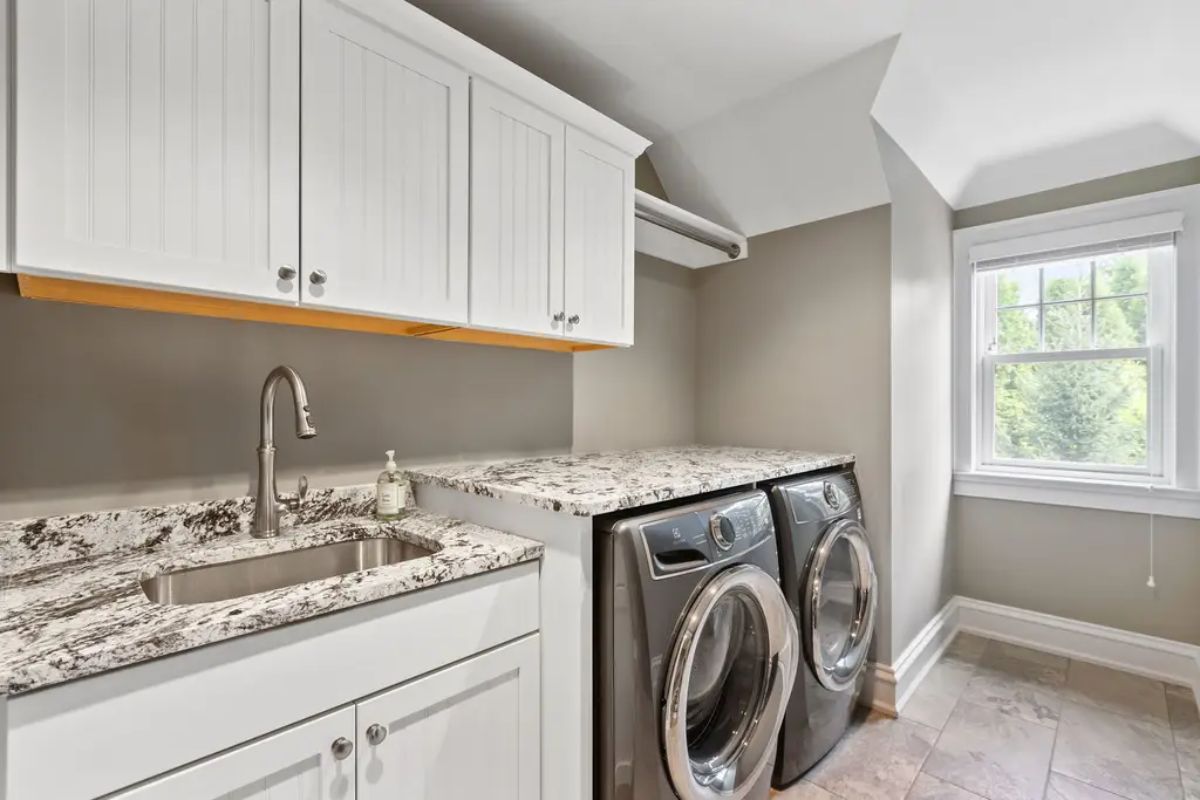 Equipped with front-loading washer and dryer units beneath a spacious granite countertop for folding and organizing laundry.