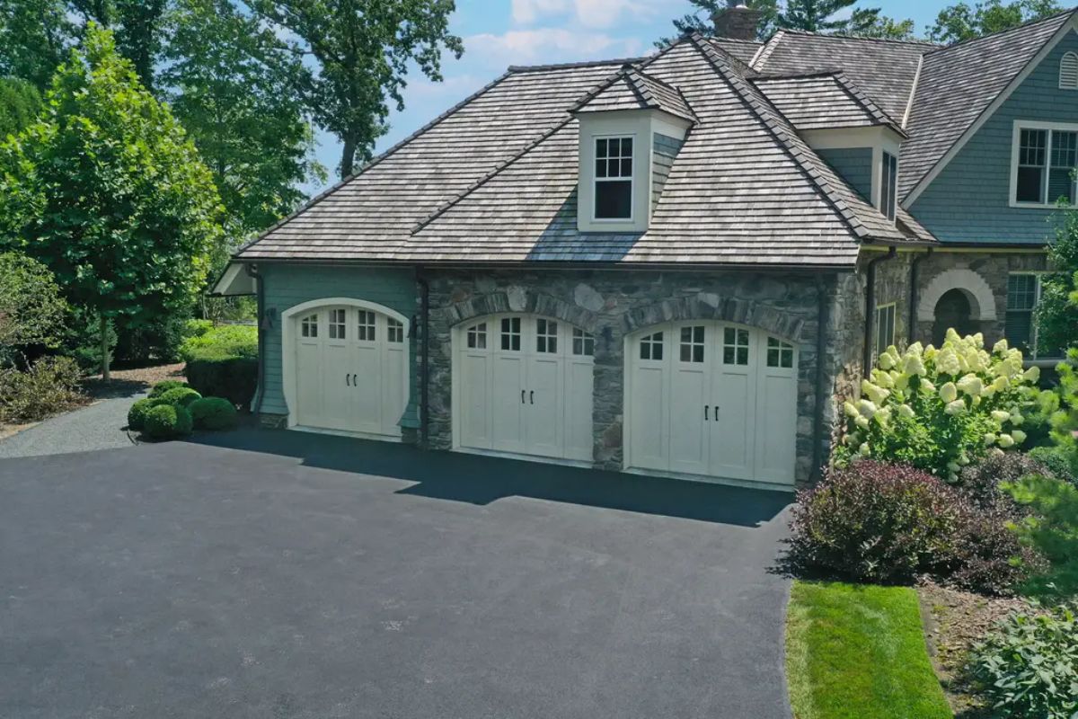 Three-car garage with white, carriage-style doors set against a stone façade.