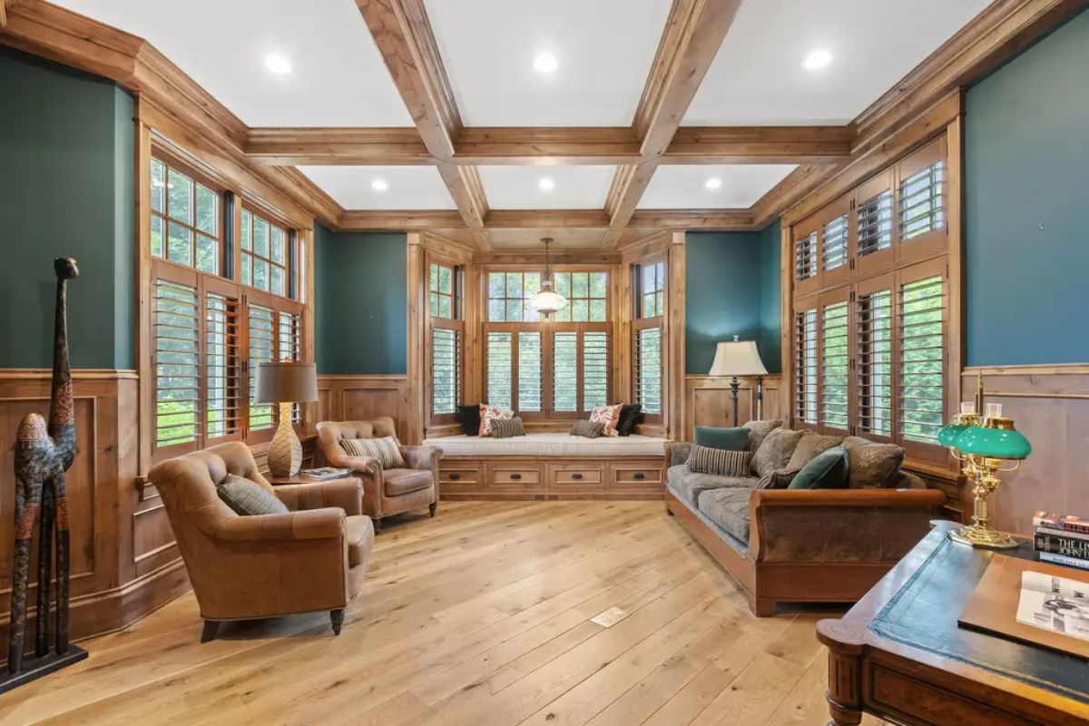 Inviting study space with rich wood paneling, coffered ceiling, and large windows fitted with plantation shutters.