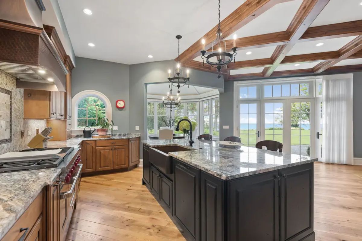 Spacious kitchen showcases natural wood cabinetry, a large black island with granite countertops, and a farmhouse sink.