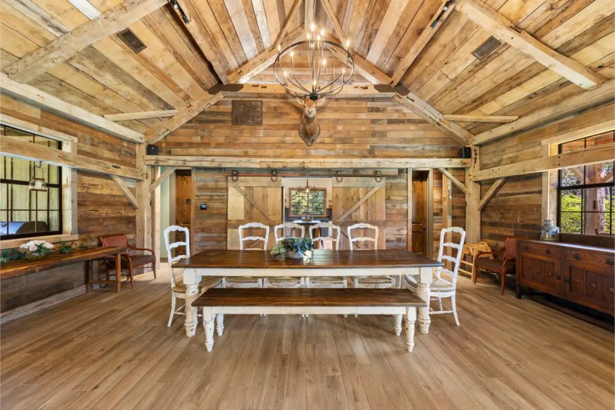 Dining room with wood-paneled walls, exposed beams, and a central chandelier.