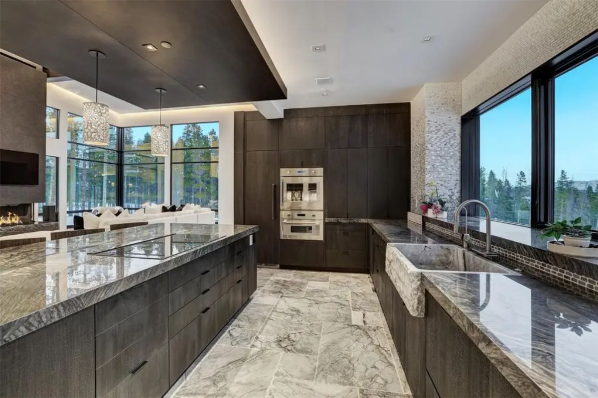 Luxury kitchen features dark cabinetry, marble countertops, and a large island, complemented by modern pendant lighting. 