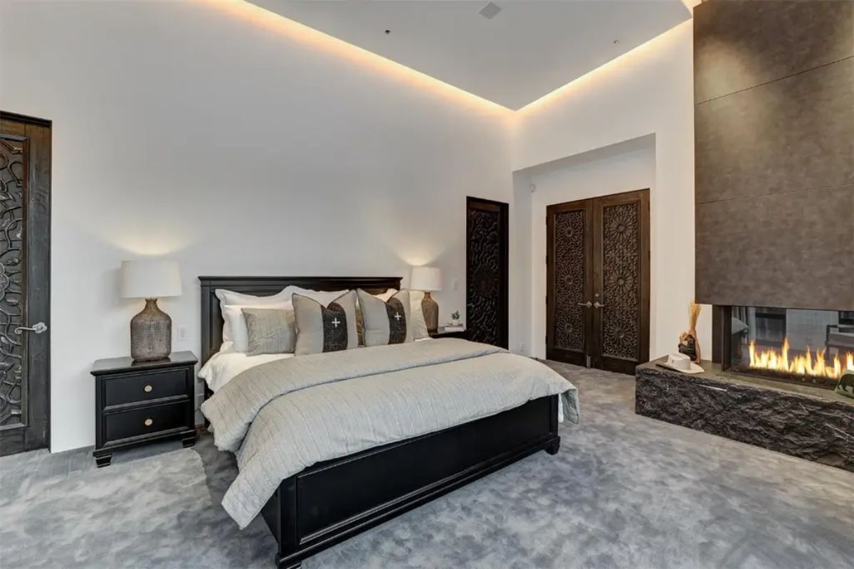 Elegant master bedroom includes a sleek fireplace, black wood furniture, and soft recessed lighting for a warm atmosphere. 