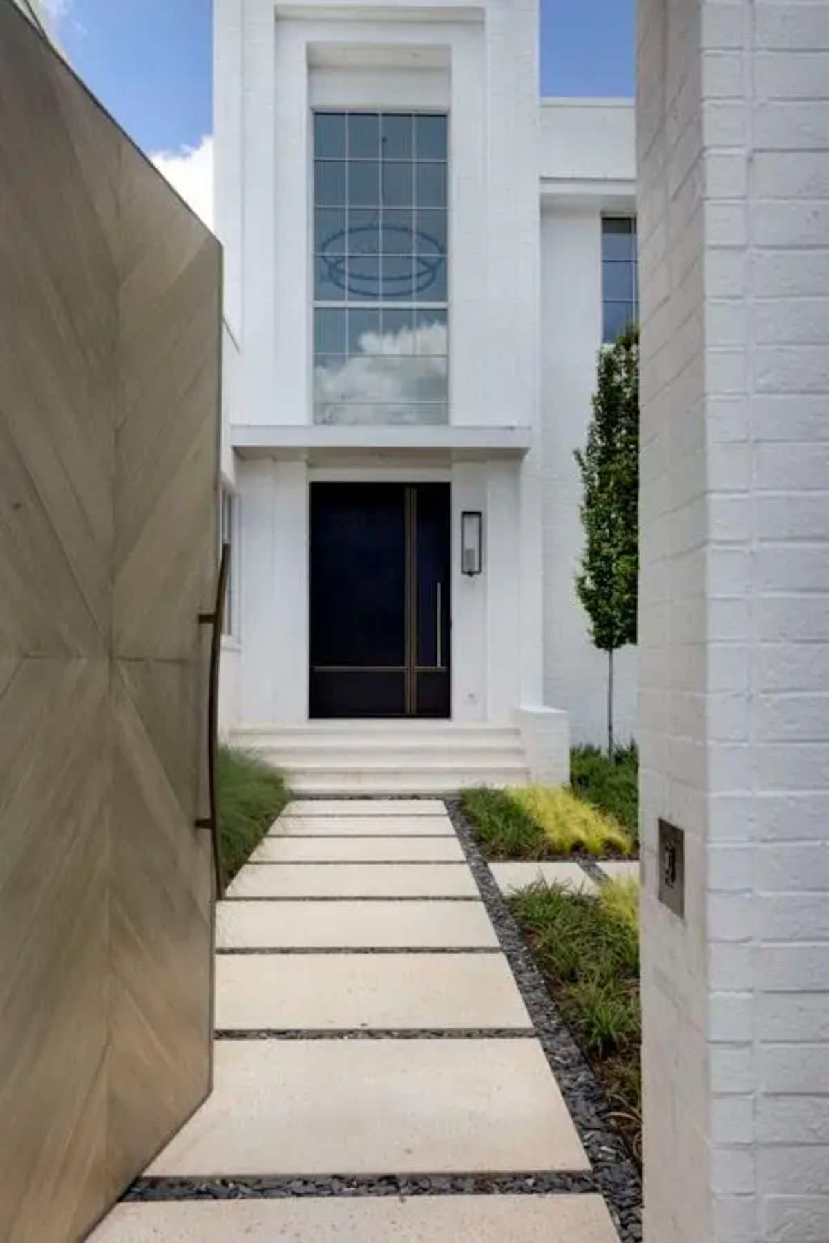 Close-up of the entrance pathway leading to a black double-door entrance framed by tall windows and a white brick facade. 