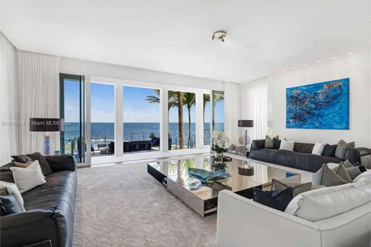 Bright living room with floor-to-ceiling windows offering breathtaking ocean views, stylish black and white seating, and modern art. 