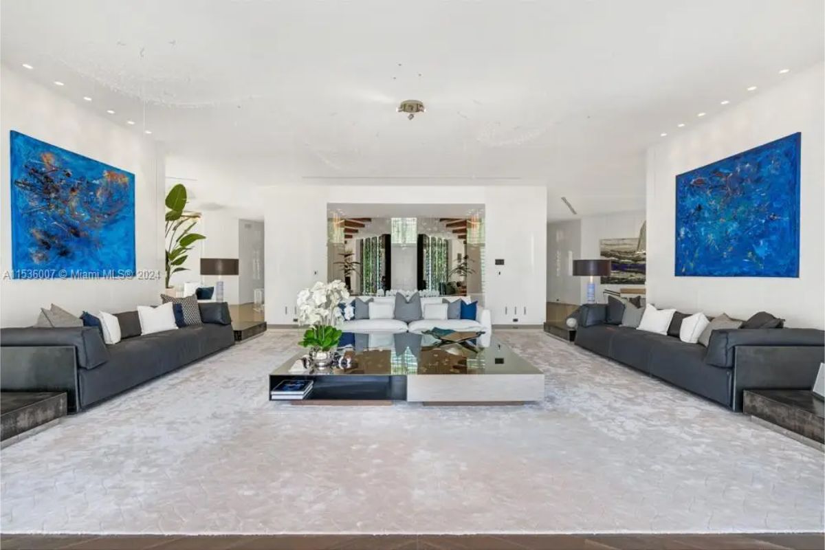 Spacious living area with contemporary décor, large gray sofas, mirrored coffee table, and bold blue artwork accentuating the white walls. 