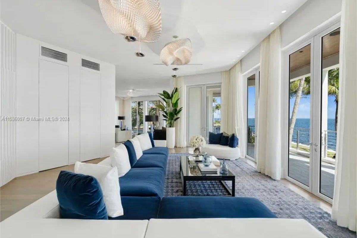 Chic lounge with plush blue seating, glass coffee table, and expansive windows showcasing panoramic ocean views. 