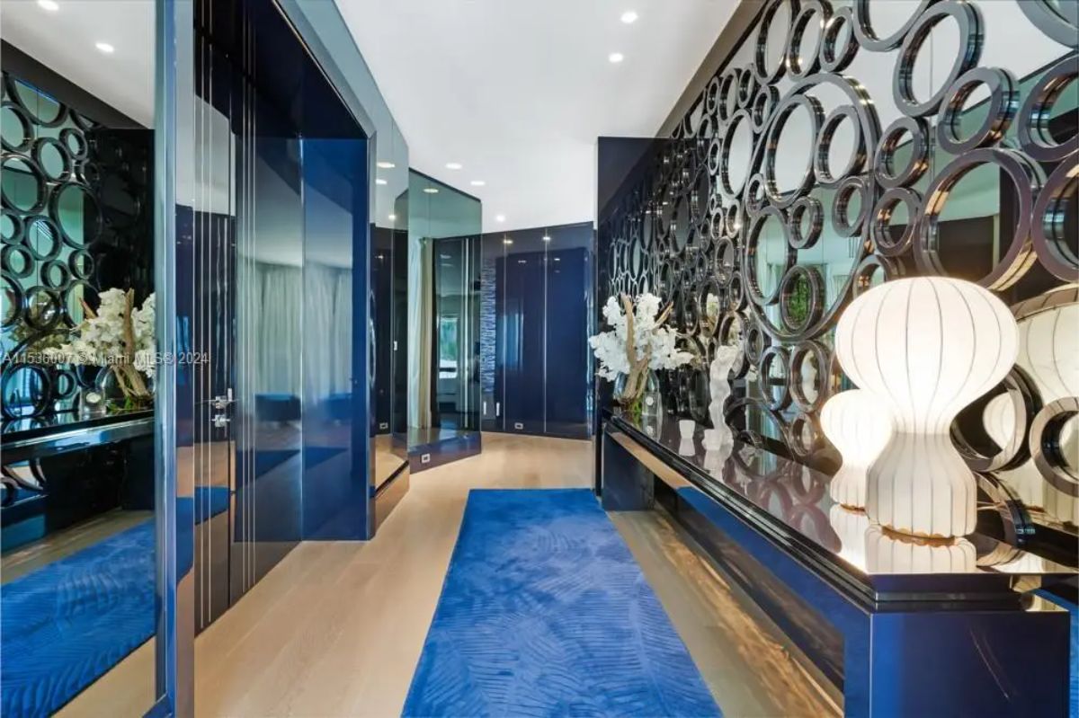 Vibrant hallway adorned with circular mirrored wall accents, glossy blue panels, and contemporary white sculptural lamps on a reflective console table. 