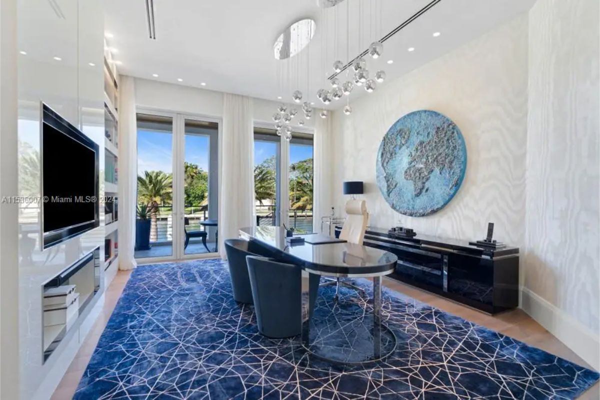 Home office includes a black desk, modern light fixtures, a large circular map on the wall, and access to a balcony with water views. 