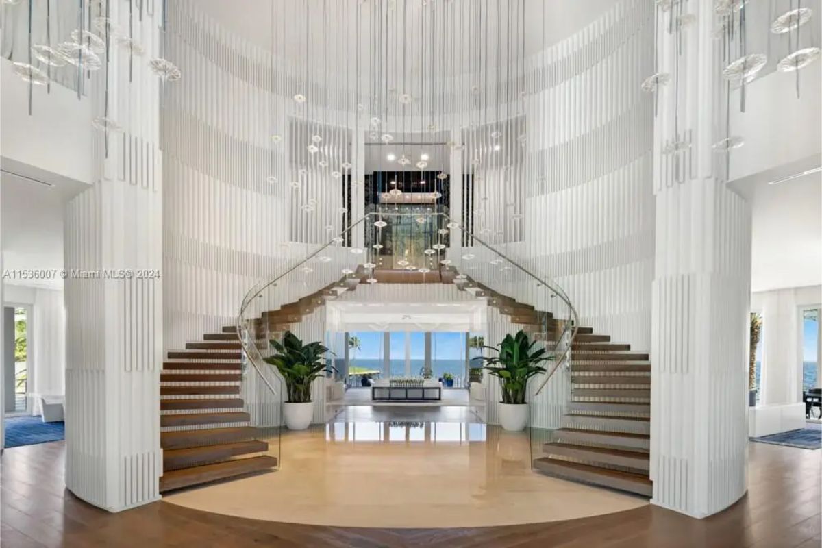 Sophisticated double staircase foyer with modern design elements, hanging light fixtures, and ocean views in the background. 