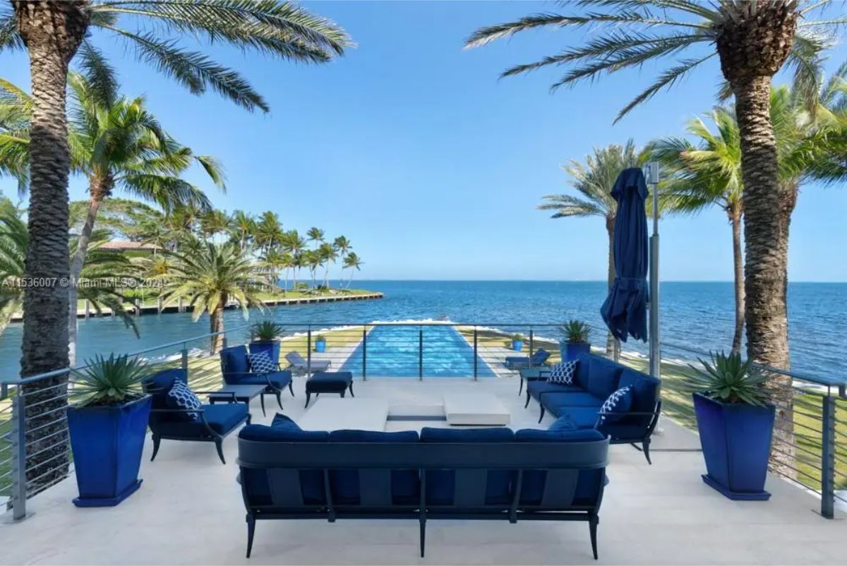 Outdoor terrace has navy blue seating arrangements, potted plants, and overlooks an infinity pool with an ocean backdrop. 