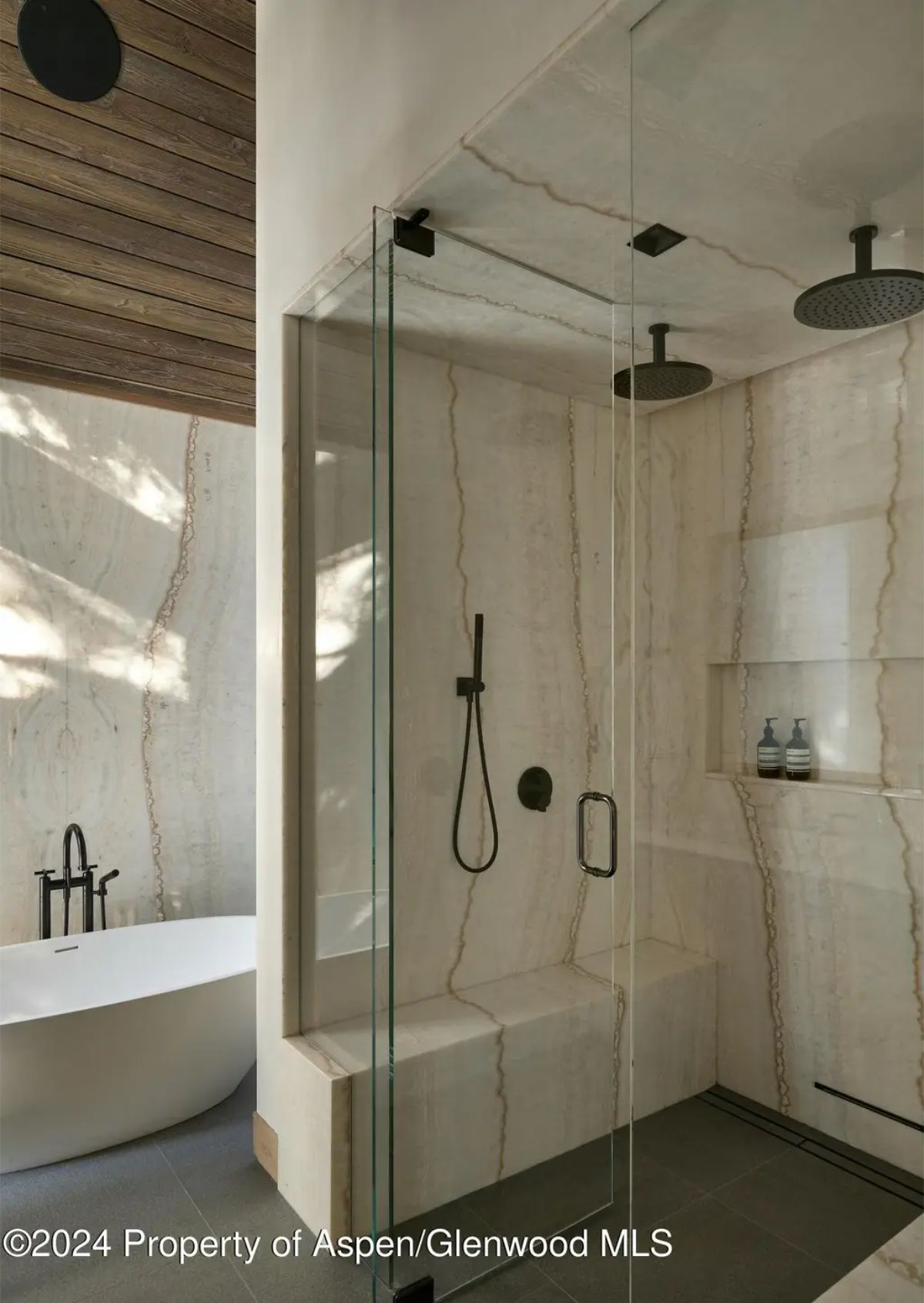 Sophisticated shower space incorporates dual rainfall showerheads, sleek black fixtures, and marble wall detailing. 