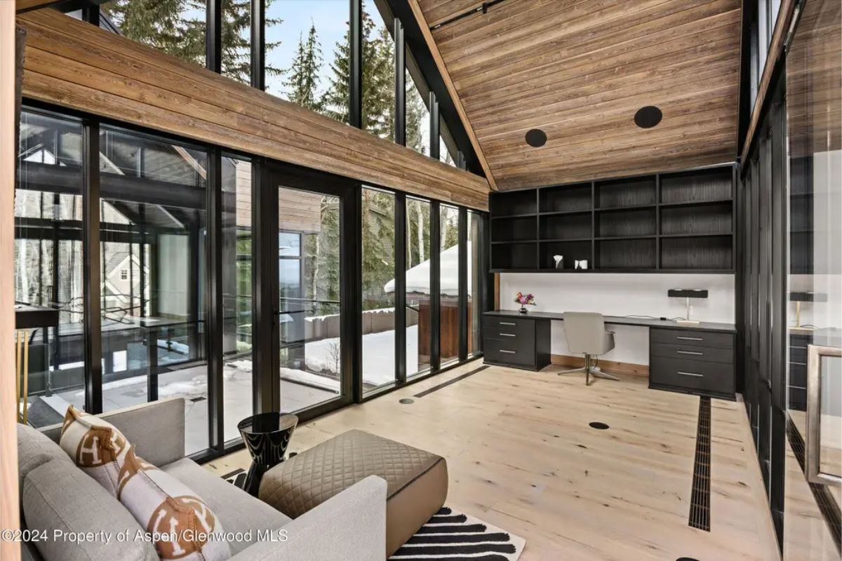 Contemporary home office includes an open-concept design, black built-in shelving, and panoramic floor-to-ceiling windows. 