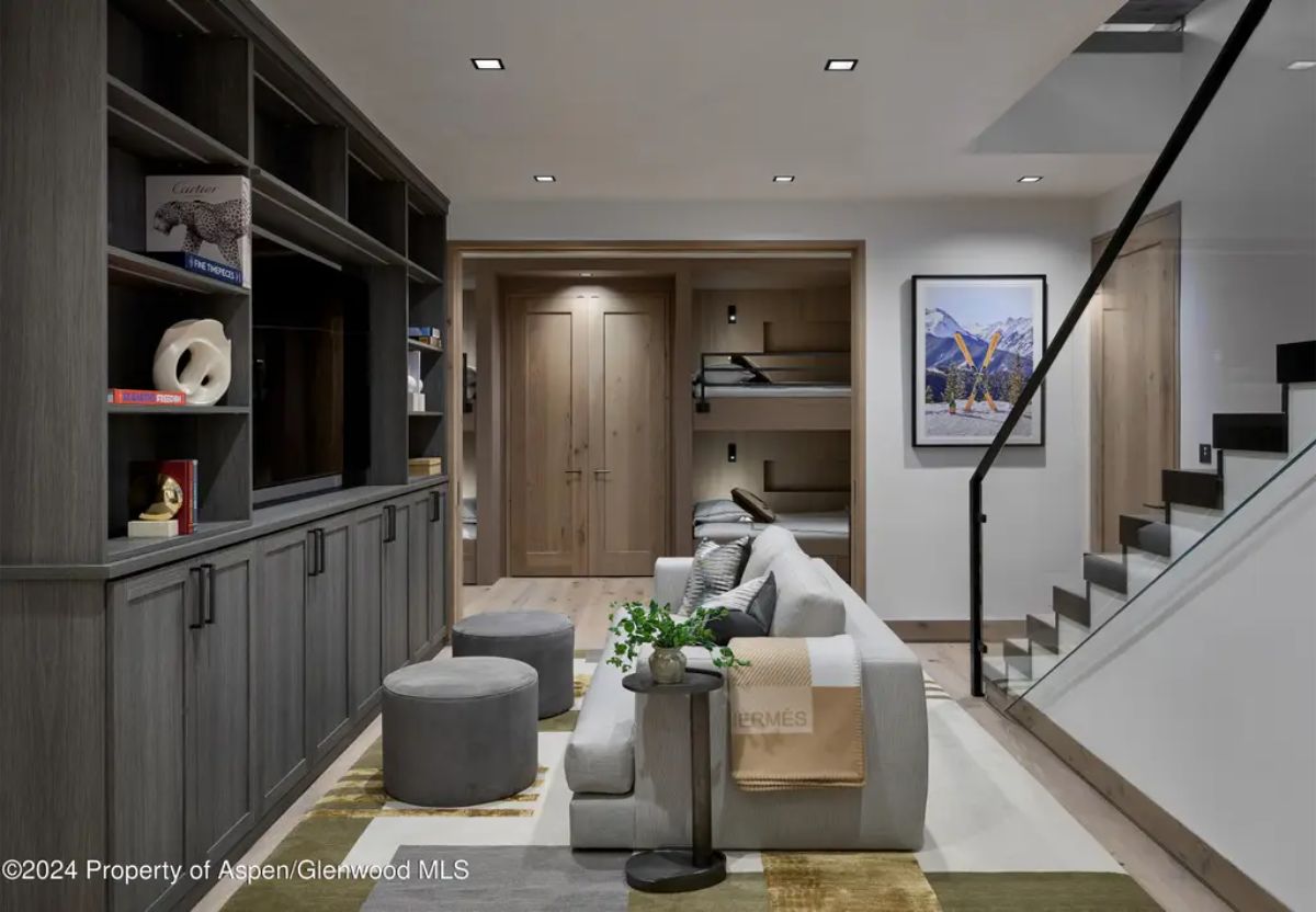 Stylish media room with built-in shelves, a plush sectional, and a bunk nook in the background. 