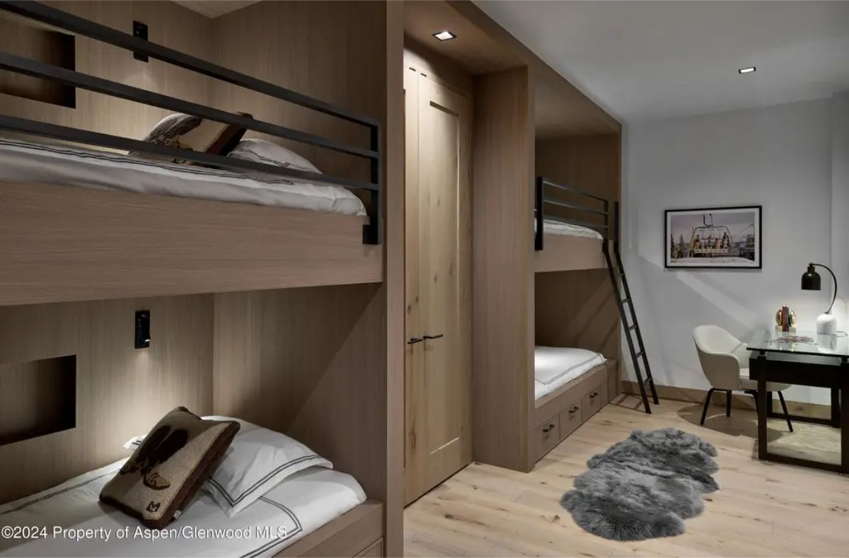 Stylish bunk room contains built-in wooden beds, soft lighting, and a small desk setup for work or study. 